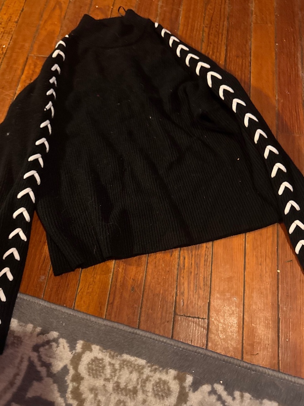 Classic black sweater with contrasting white lace-style trim along each sleeve.
